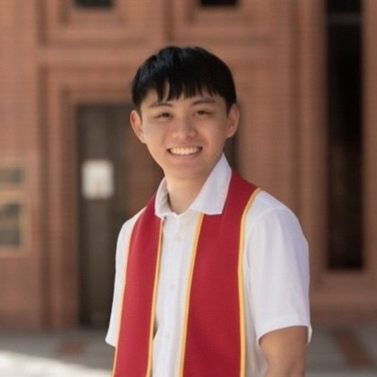 Kyler Saiki, smiling, in a white shirt in front of a brick building.
